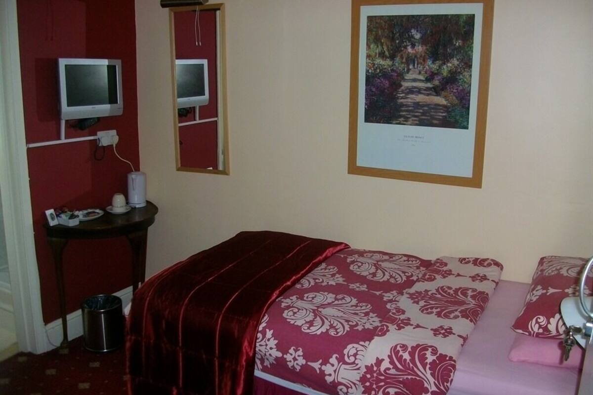 A bedroom with a bed, a desk, a chair, and a television.