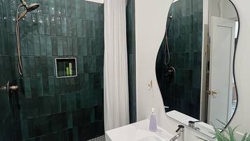 A modern bathroom with a shower, a sink, a mirror, and a potted plant.