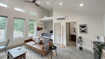 A spacious living room with a high ceiling, a ceiling fan, and large windows offering a view of the outdoors.