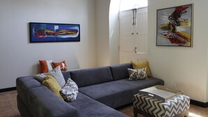 A modern living room with a grey sectional sofa, a small wooden table, and two artworks on the walls.