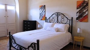 A neatly made bed with white linens, a black metal headboard, and two wall-mounted paintings.