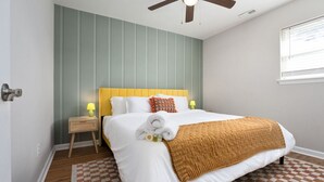 Ein Schlafzimmer mit Bett, Nachttisch, Deckenventilator, Fenster und einem gemusterten Teppich.