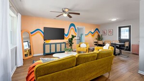 Ein Wohnzimmer mit Sofa, Fernseher, Deckenventilator und einer Essecke mit Stühlen und Tisch.