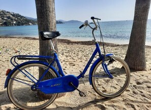 A blue electric bike parked on a sandy beach with a view of the sea and hills in the background.