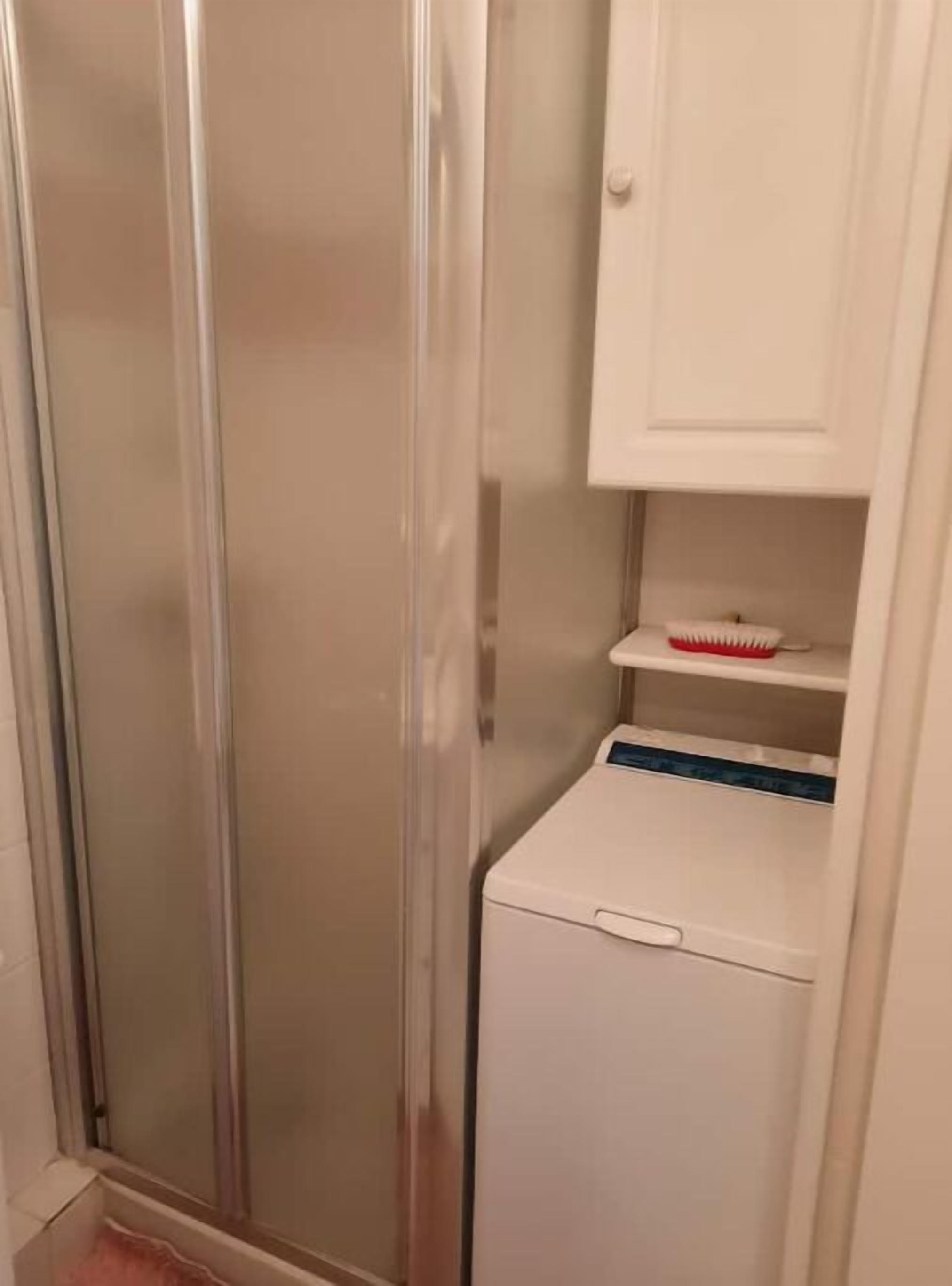 Une salle de bain avec une douche à parois de verre, un meuble blanc avec une brosse à dents, et un lave-linge blanc.