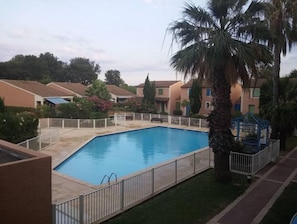 Una piscina circondata da una recinzione, con palme e case sullo sfondo.