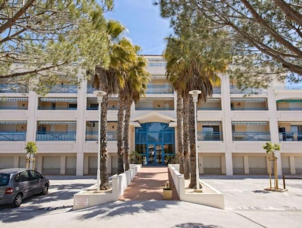 A multi-story hotel with a central entrance, palm trees, and a car parked in front.