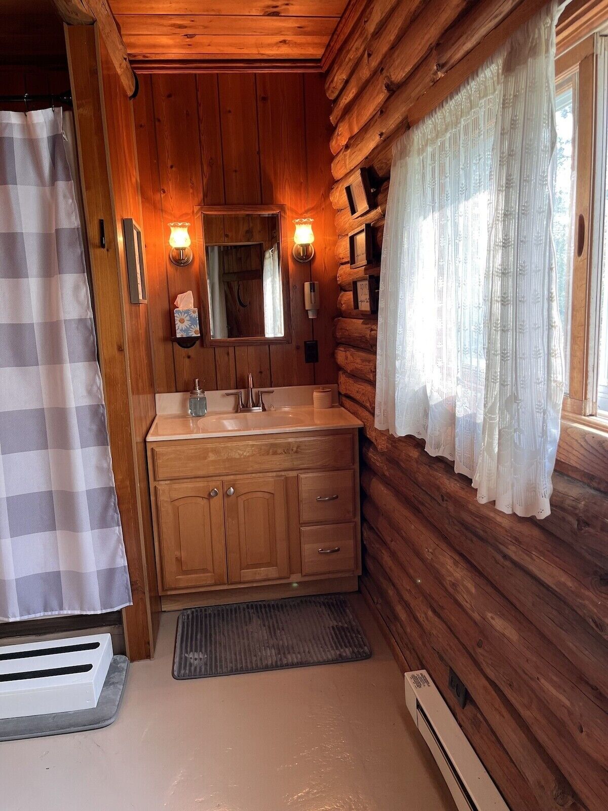 A log cabin bathroom with wooden walls, a wooden vanity, a sink, a mirror, a towel rack, and a window with sheer curtains.