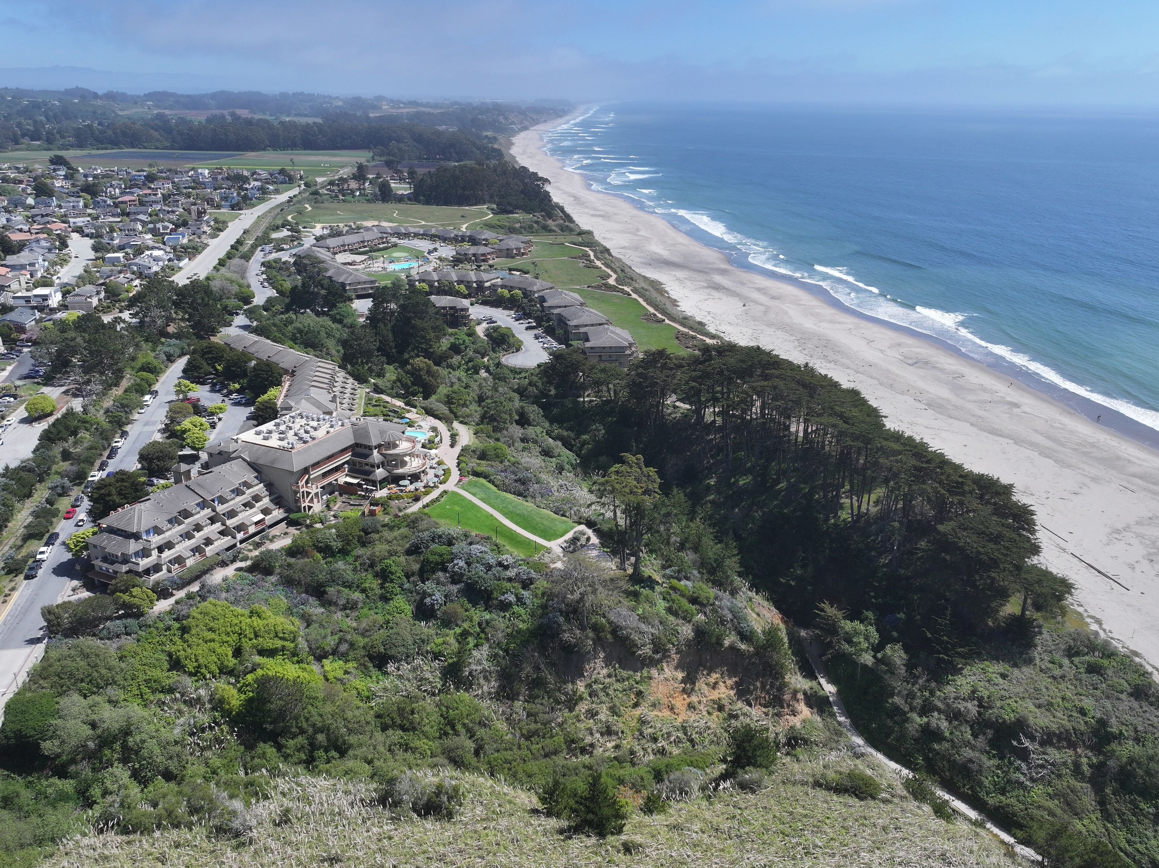 An aerial view of a coastal resort with a beachfront, a pool area, and a golf course.