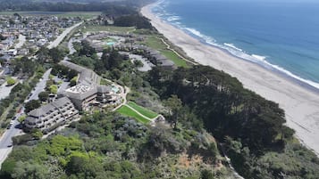 An aerial view of a coastal resort with a beachfront, a pool area, and a golf course.