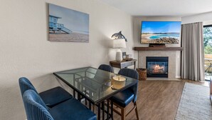 Una sala moderna con una mesa de comedor de vidrio, asientos cómodos, una chimenea y una televisión grande mostrando una escena de playa.