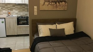 A bedroom with a bed, pillows, a painting of horses, a kitchenette with a microwave, and a small refrigerator. - Amazing Studio Next to all City Attractions (Thessaloniki)