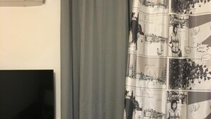 A bathroom with a grey shower curtain, a mounted flat-screen TV, and a white radiator. - Amazing Studio Next to all City Attractions (Thessaloniki)