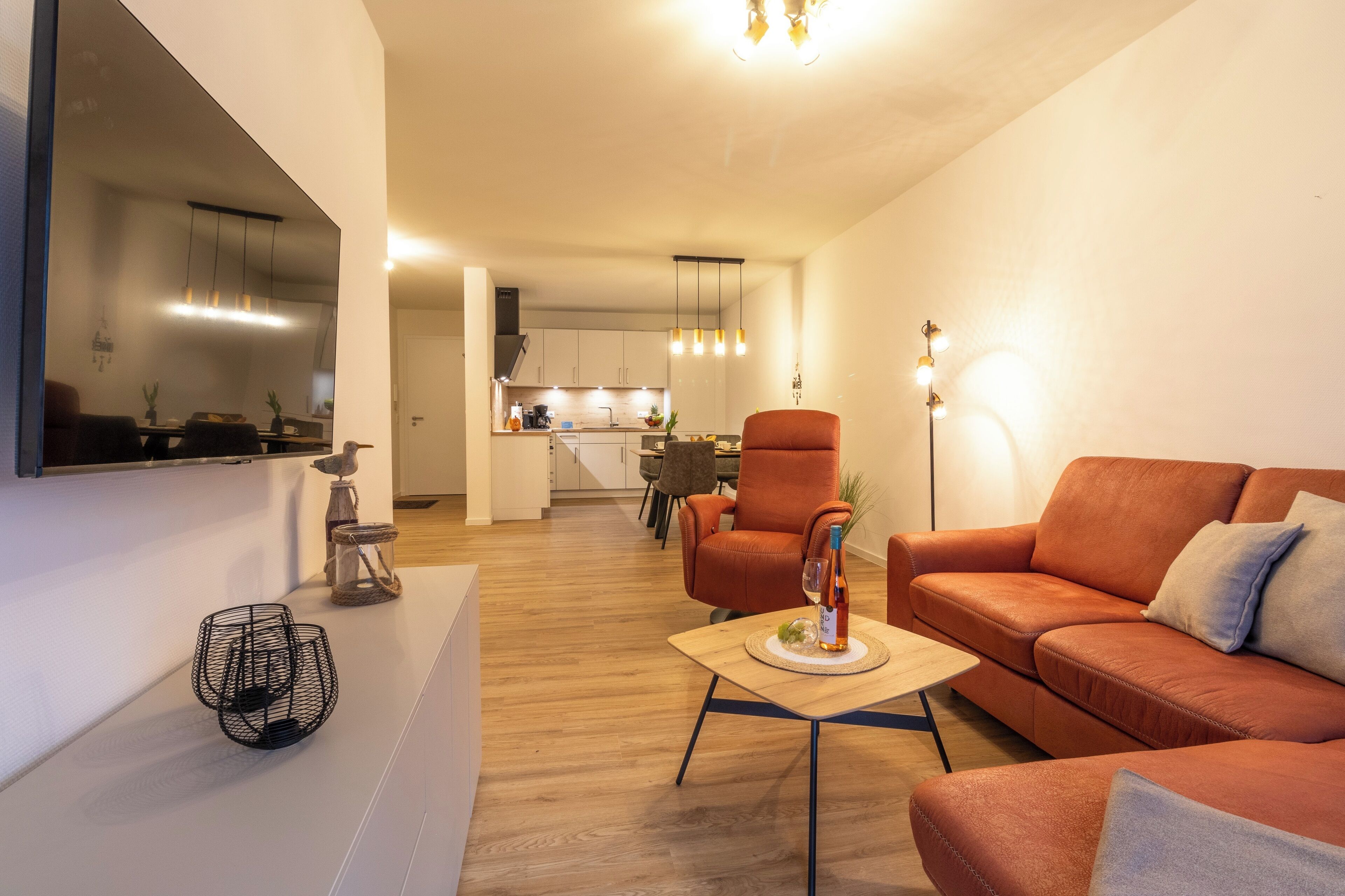 A modern living room with a sofa, armchair, and coffee table. A kitchen is visible in the background.