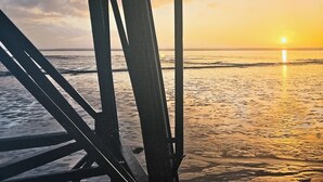 A beach view with a sunset, a pier structure, and calm sea.