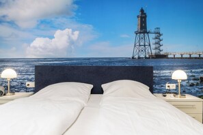A bed with white linens, two bedside lamps, and a view of a lighthouse and pier.
