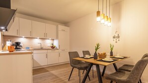 A modern kitchen with white cabinets, a wooden countertop, and a dining area with a wooden table and grey upholstered chairs.