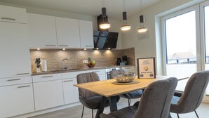 A modern kitchen with white cabinets, a wooden countertop, and a dining area with a wooden table and four grey chairs. - Dorumer Sielhuus 13 mit Sauna und Balkon (Dorum-Neufeld)
