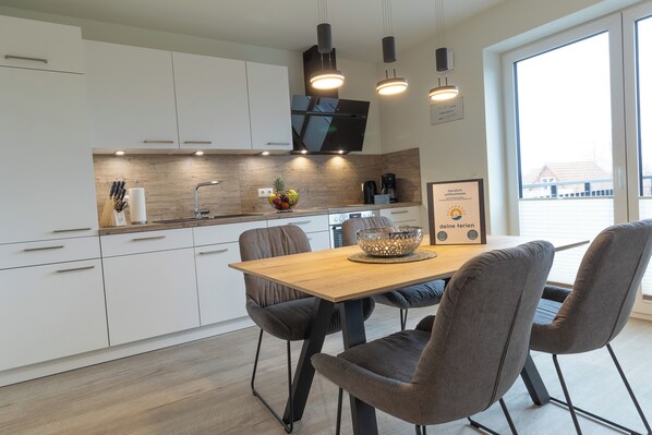 Eine moderne Küche mit weißen Schränken, einer Holz Arbeitsplatte und einem Essbereich mit einem Holztisch und vier grauen Stühlen.