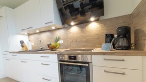A modern kitchen with white cabinets, stainless steel appliances, and a wooden countertop. - Dorumer Sielhuus 13 mit Sauna und Balkon (Dorum-Neufeld)