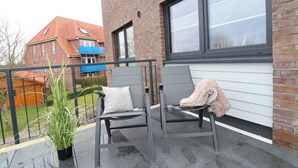A balcony with two grey chairs, a potted plant, and a fluffy pink blanket. - Dorumer Sielhuus 13 mit Sauna und Balkon (Dorum-Neufeld)