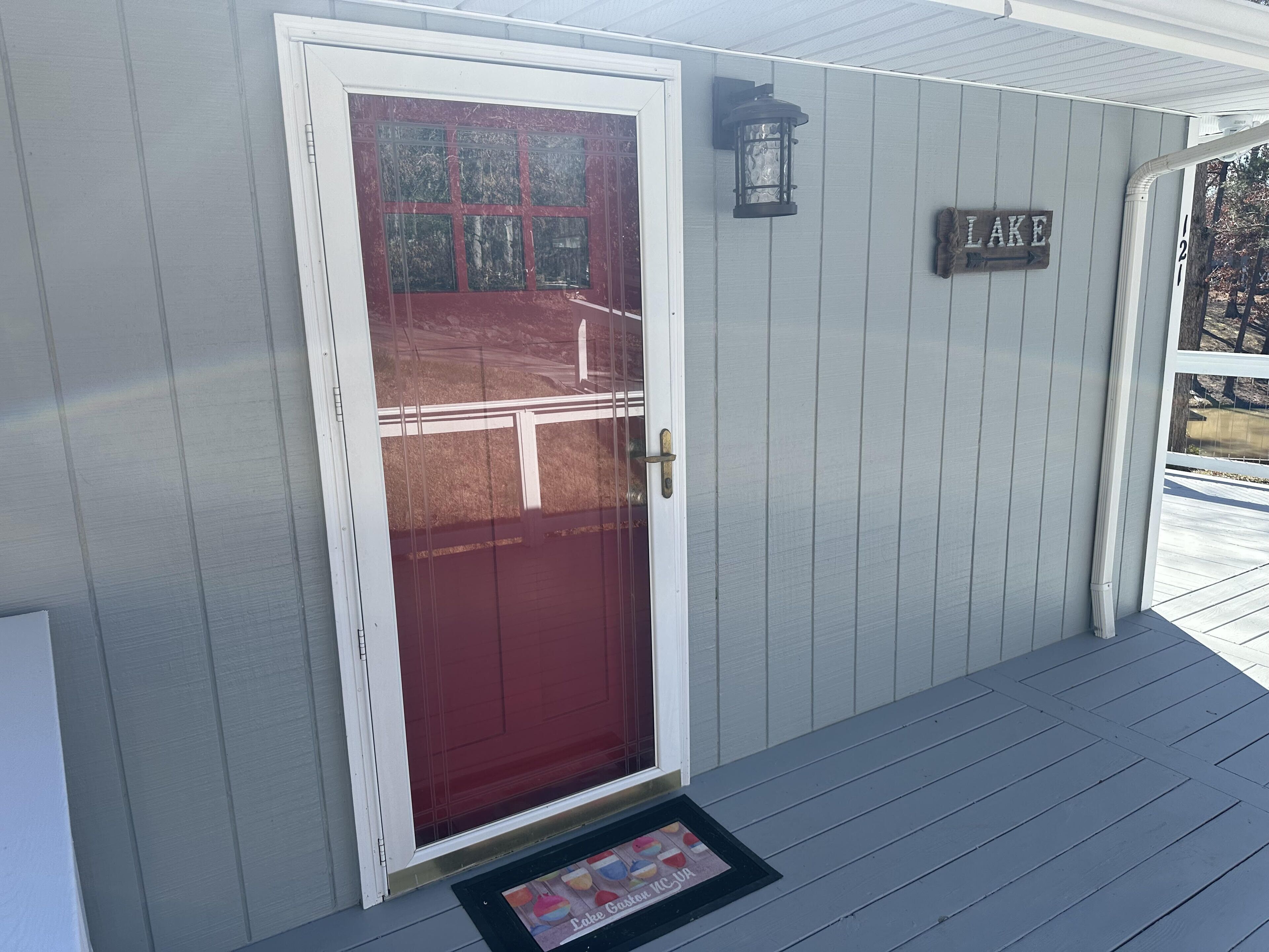 Una casa con puerta roja, un cartel que dice "LAKE" y un pequeño porche.