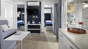 Una habitación compacta y moderna con sofá, una mesita, televisión y una zona de kitchenette.