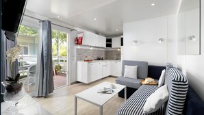 Una sala de estar moderna con un sofá y una mesa de centro, una cocina con armarios blancos y un ventanal corredero que da a un espacio exterior.