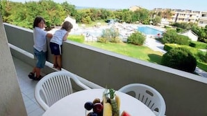 A balcony with a table set with fruit and a watermelon, overlooking a pool and greenery.