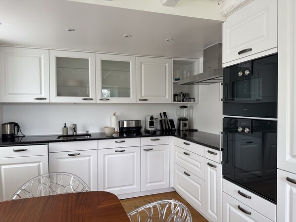 A modern kitchen with white cabinets, black appliances, and a wooden dining table.
