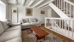 A living room with a sofa, a coffee table, and a staircase with white railings. - domaine du deven (Bourg-en-Lavaux)