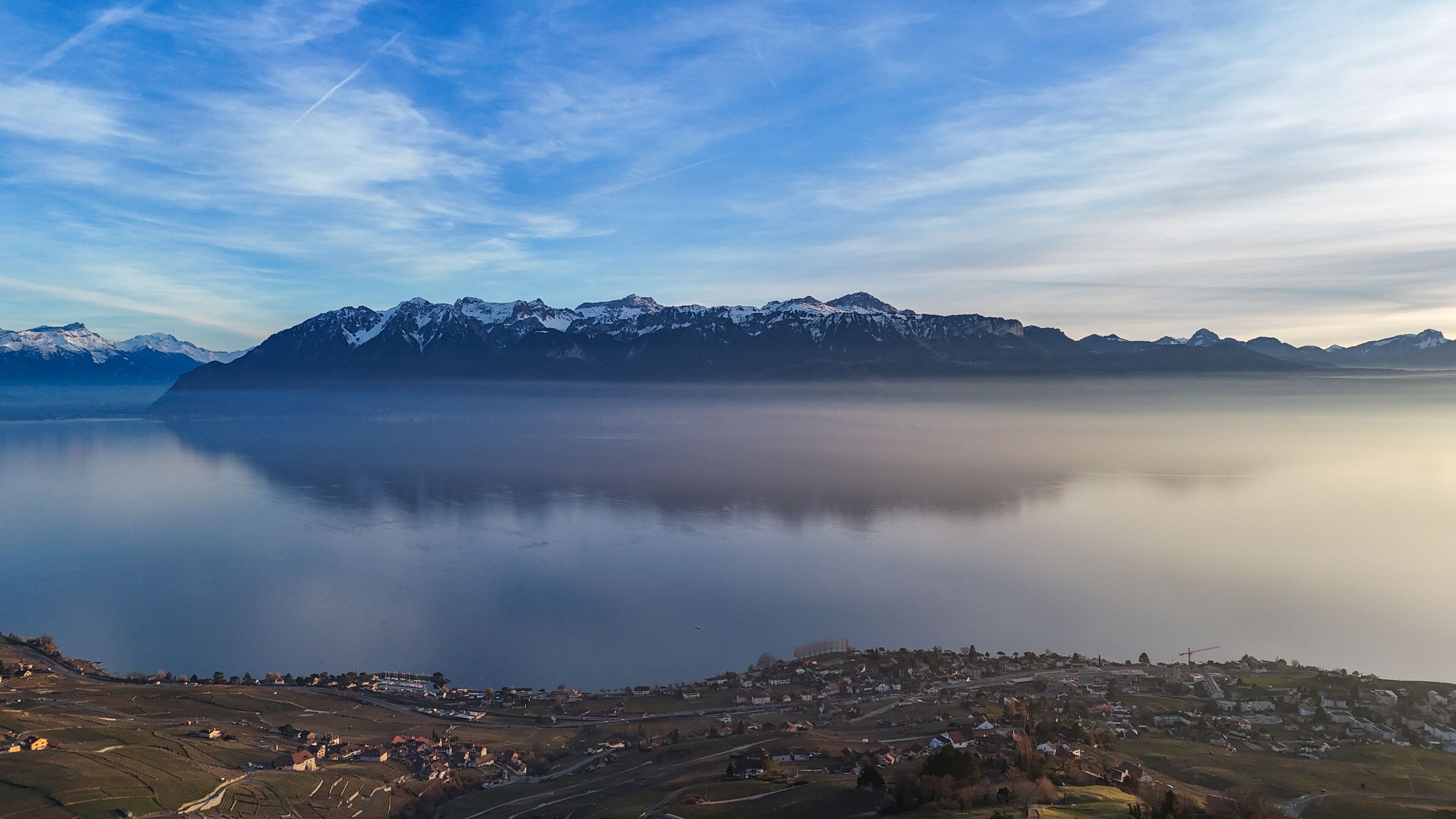 Une vue panoramique d’un paysage montagneux, avec un lac paisible et une petite ville au premier plan.