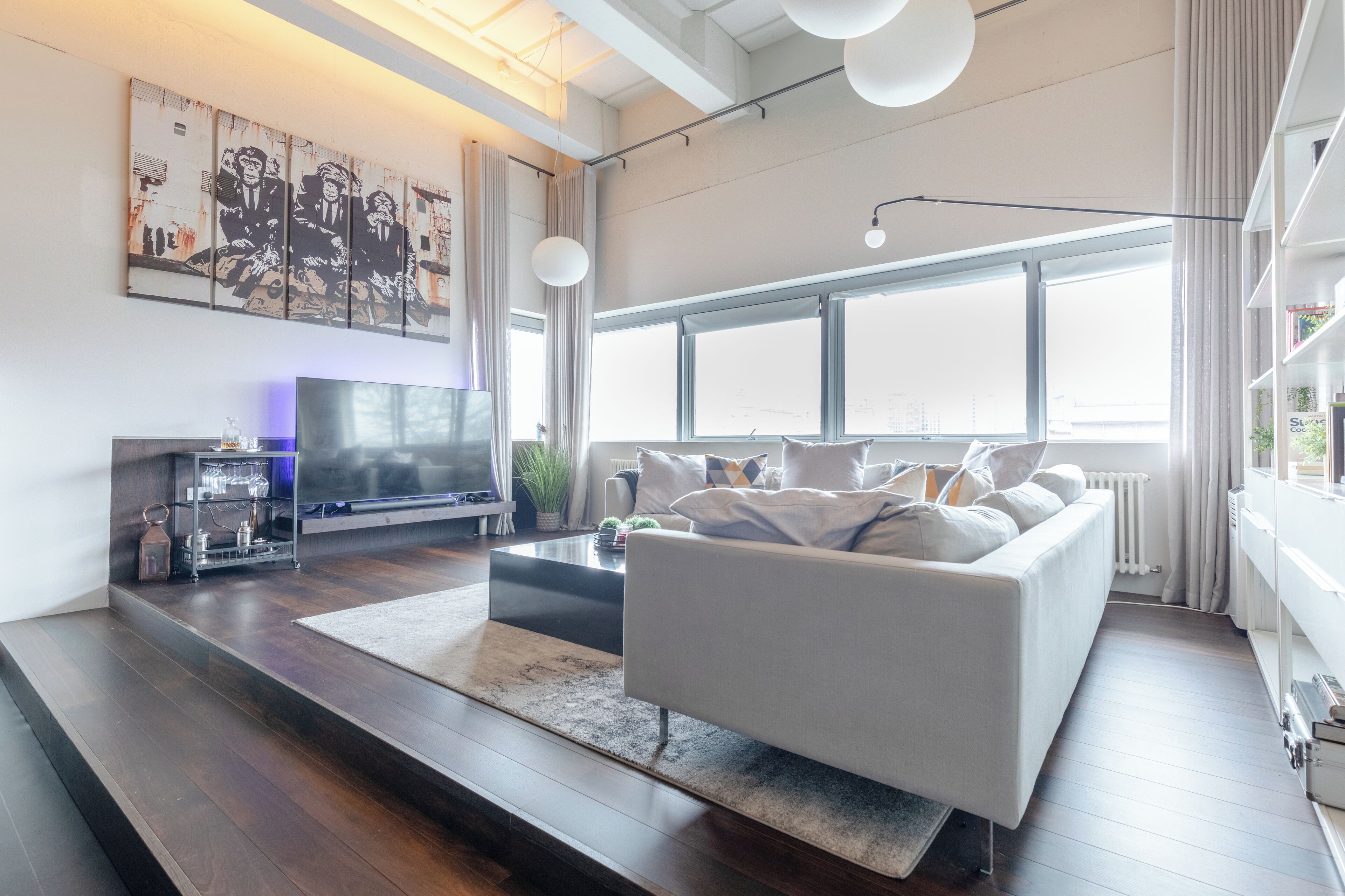 Uma sala de estar moderna, com uma janela grande, uma TV de tela plana, um sofá branco e uma mesa de centro.