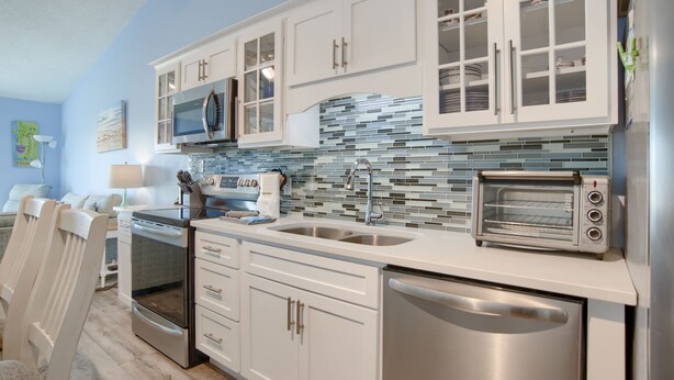 A modern kitchen with white cabinets, stainless steel appliances, and a blue-tiled backsplash.