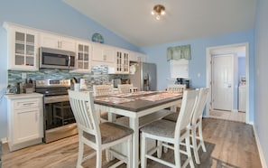 A kitchen with white cabinets, a microwave, and a refrigerator. There is a dining table with chairs and a placemat.