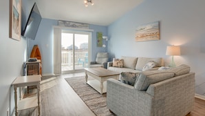 A living room with a sofa, a coffee table, a TV, and a view of the beach through a sliding door.