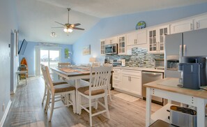 A modern kitchen with white cabinets, a microwave, and a coffee maker. There is a dining table with chairs and a ceiling fan.