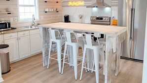 Une cuisine moderne avec un îlot central en bois, des tabourets de bar blancs, des appareils en acier inoxydable et des luminaires suspendus.