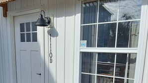 Un bâtiment blanc doté d’une terrasse en bois, d’un toit en métal et d’une fenêtre donnant sur l’intérieur.