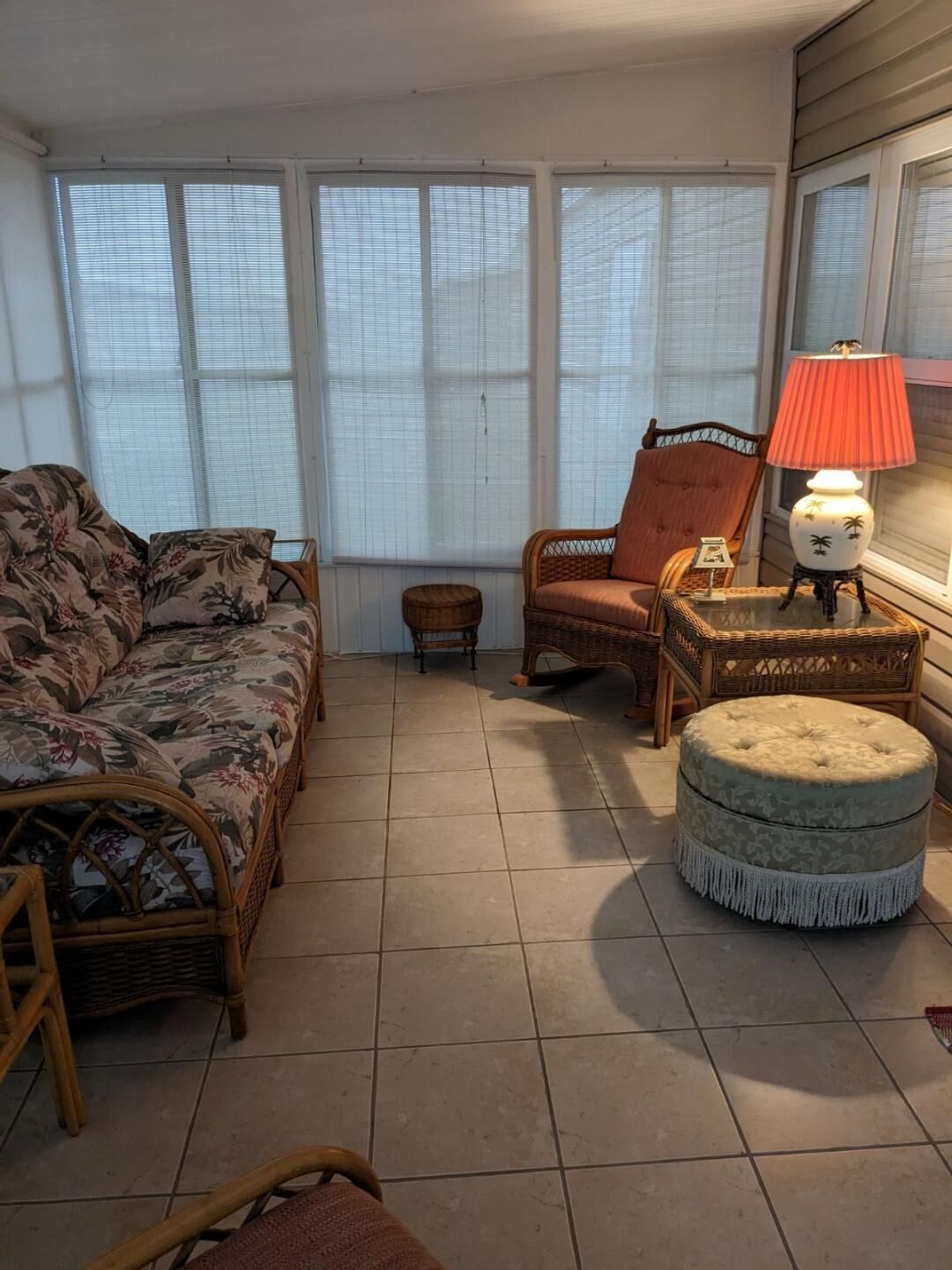 Un salon confortable avec un canapé, un fauteuil, un petit pouf et une table avec une lampe.