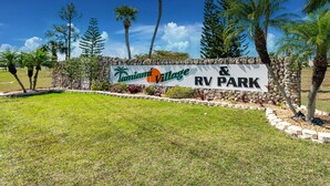 A sign for Tamiami Village RV Park with a stone wall and palm trees.