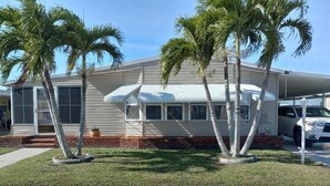 A two-story house with a covered porch, palm trees, and a parked car.