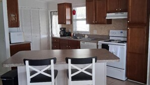 A kitchen with wooden cabinets, a central island with bar stools, a ceiling fan, and a stove.