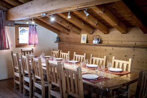 Een houten eetkamer met een hoge plafond, zichtbare balken, en een tafel gedekt voor zes personen met stoelen.