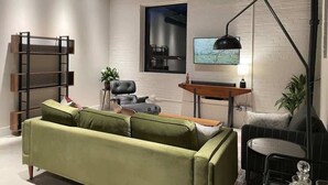Ein modernes Wohnzimmer mit einem grünen Sofa, einem schwarzen Sessel, einem kleinen runden Tisch, einem Fernseher und einer Lampe.