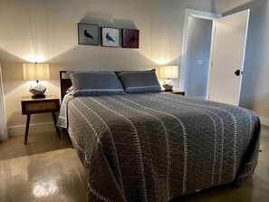 A bedroom with a bed, two bedside tables, wall-mounted lamps, and three framed pictures. - Classic Pied a Terre (Benton Harbor)