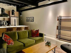 Een moderne woonkamer met een groene bank, een houten salontafel en een keuken in de achtergrond.