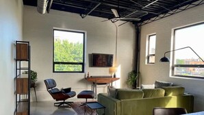 Ein modernes Wohnzimmer mit einer Couch, Sesseln, einem Couchtisch und einem an der Wand montierten Fernseher.
