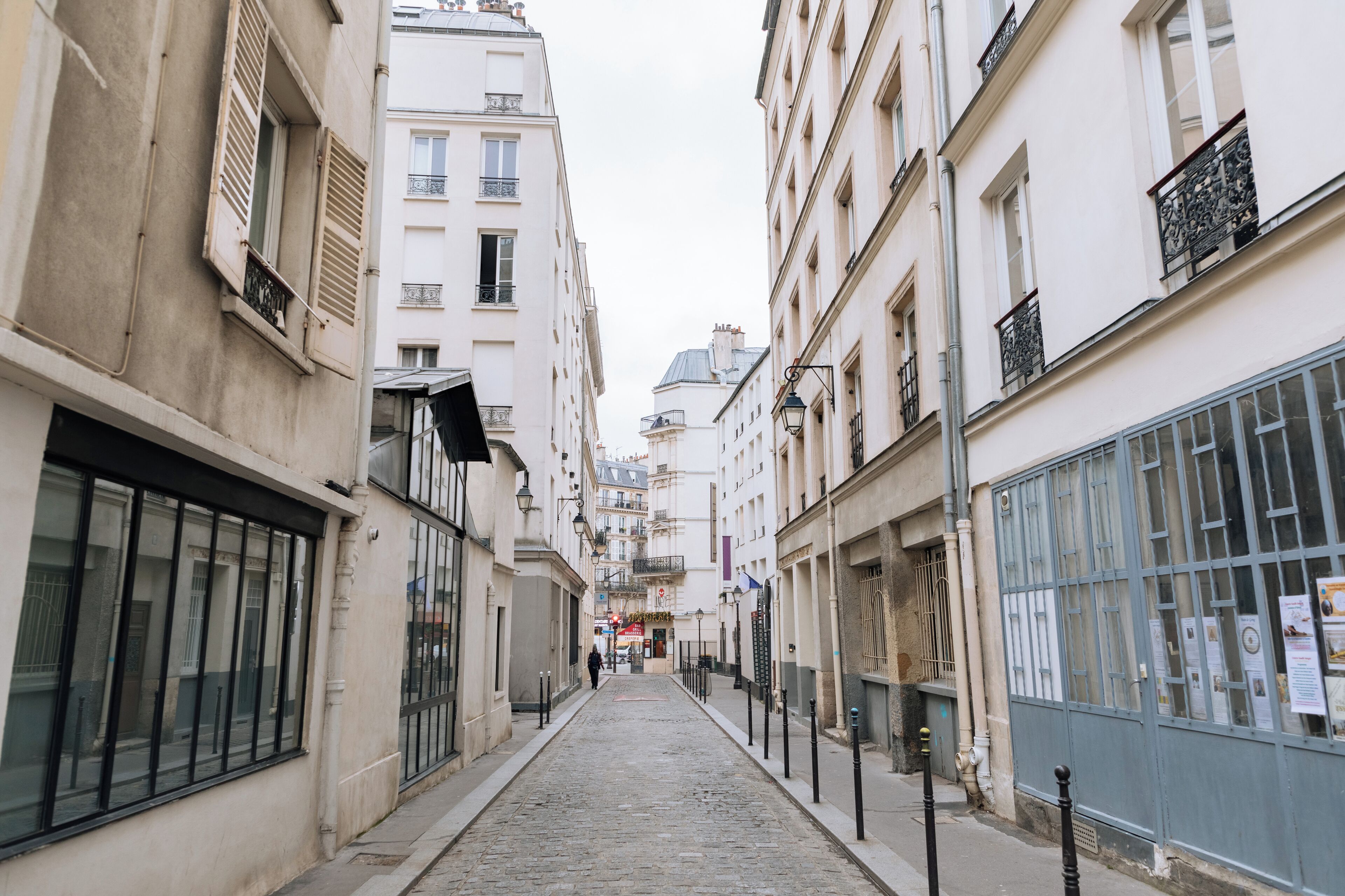 A narrow cobblestone street flanked by buildings with large windows and balconies.