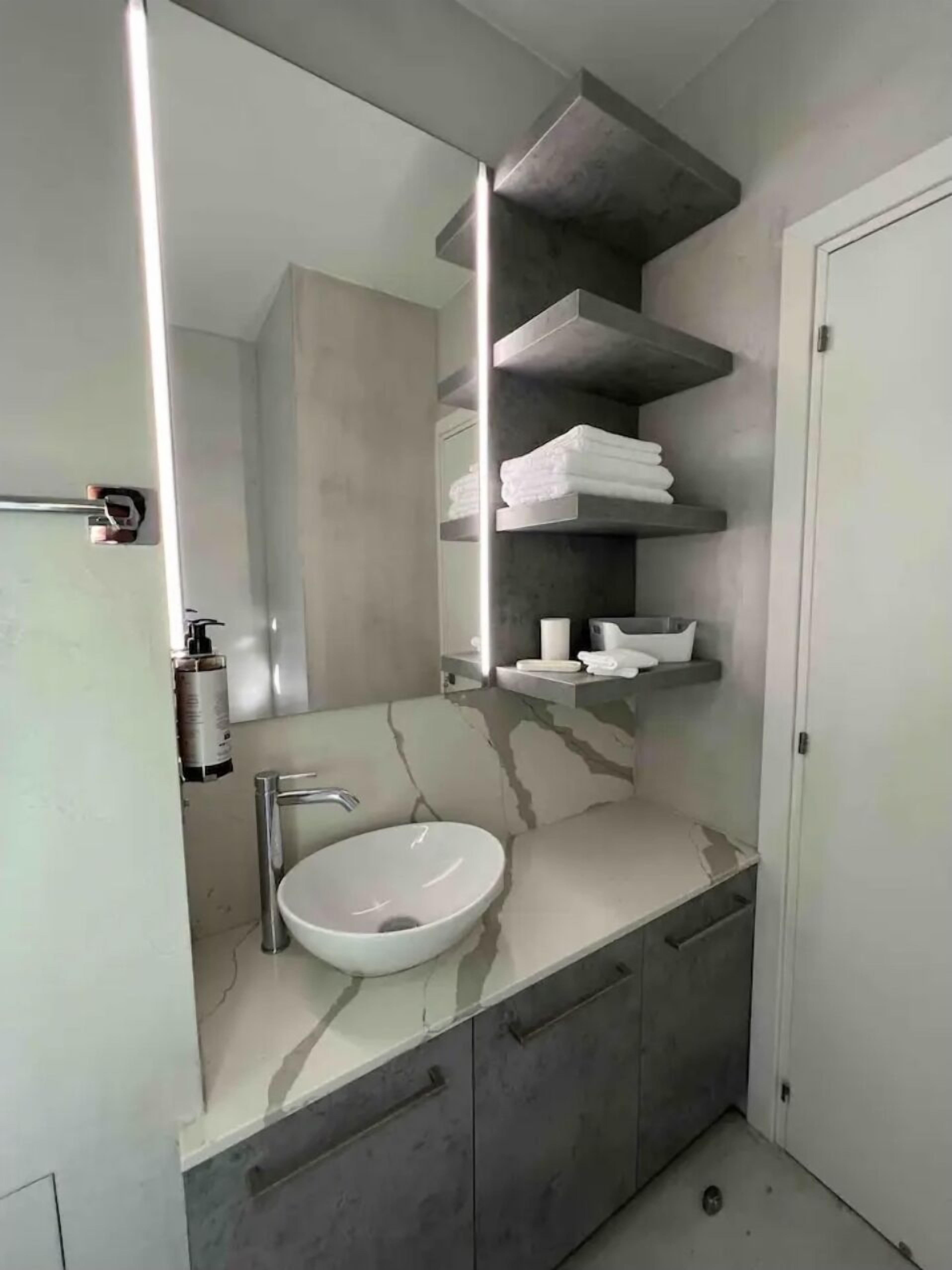 A modern bathroom with a white marble sink, a large mirror, and built-in shelves for toiletries.